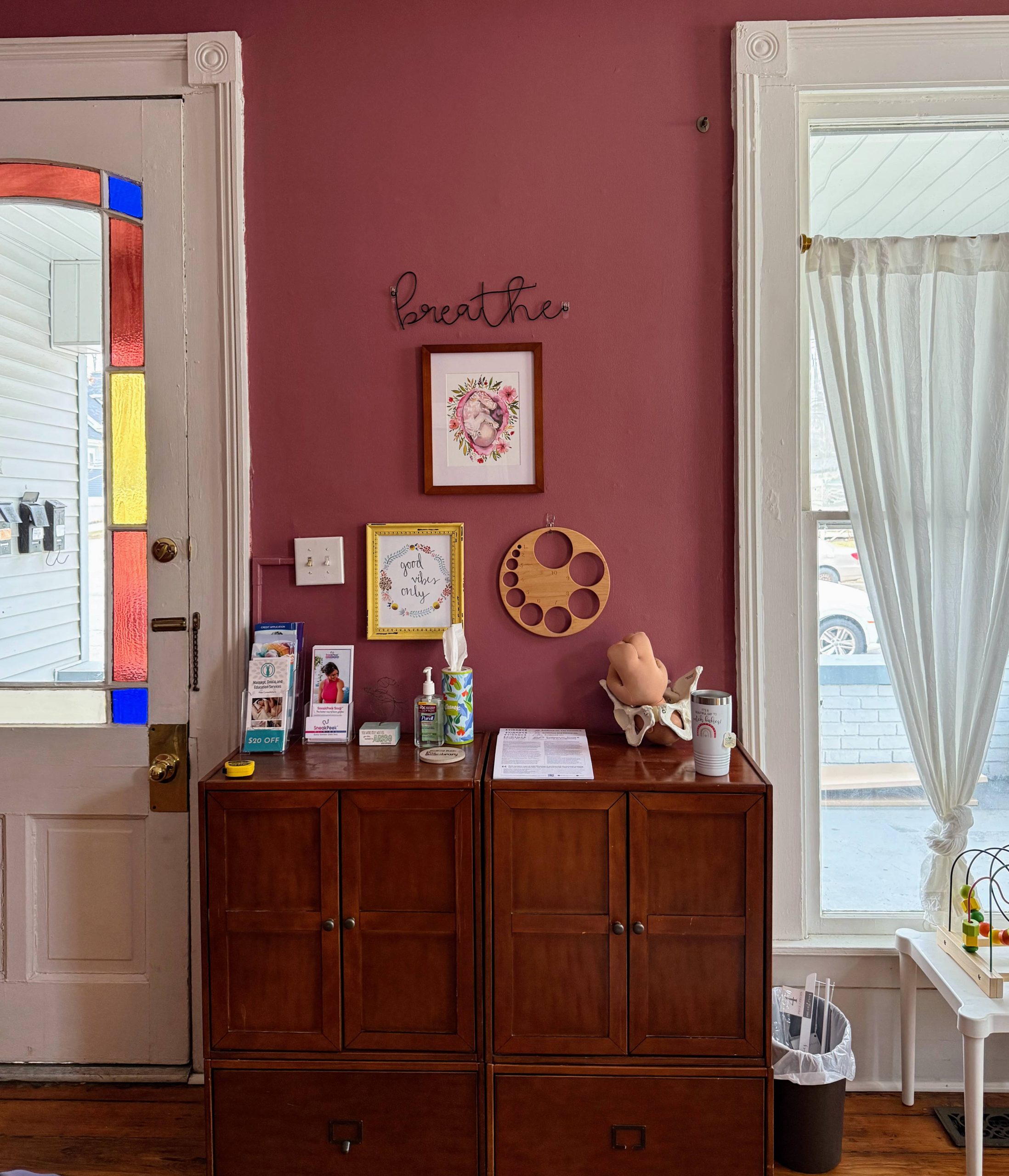 Interior welcome area of Mother Nurtured Midwifery office in Bloomington Indiana with pink wall decor and educational birth model